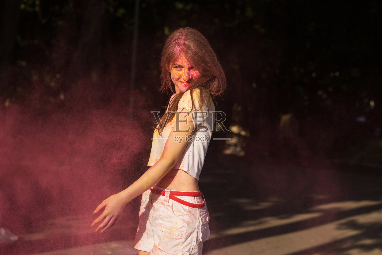 欢快的年轻模特摆着粉红色的胡里粉在她周围爆炸照片摄影图片