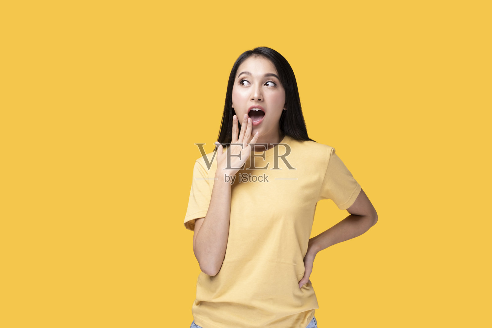 快乐的亚洲女人穿着黄色t恤站在黄色背景下。照片摄影图片