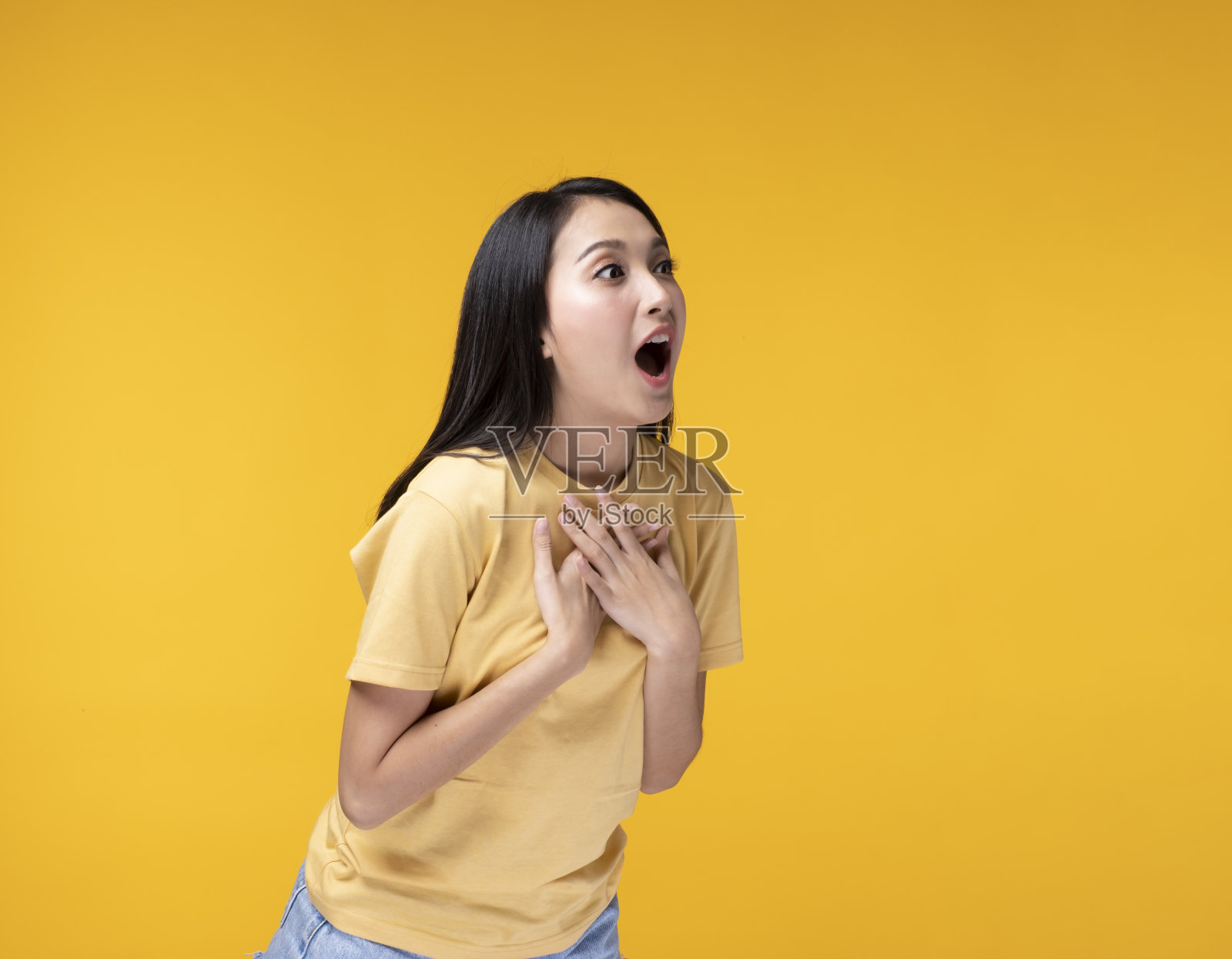 快乐的亚洲女人穿着黄色的t恤站在黄色的背景。照片摄影图片