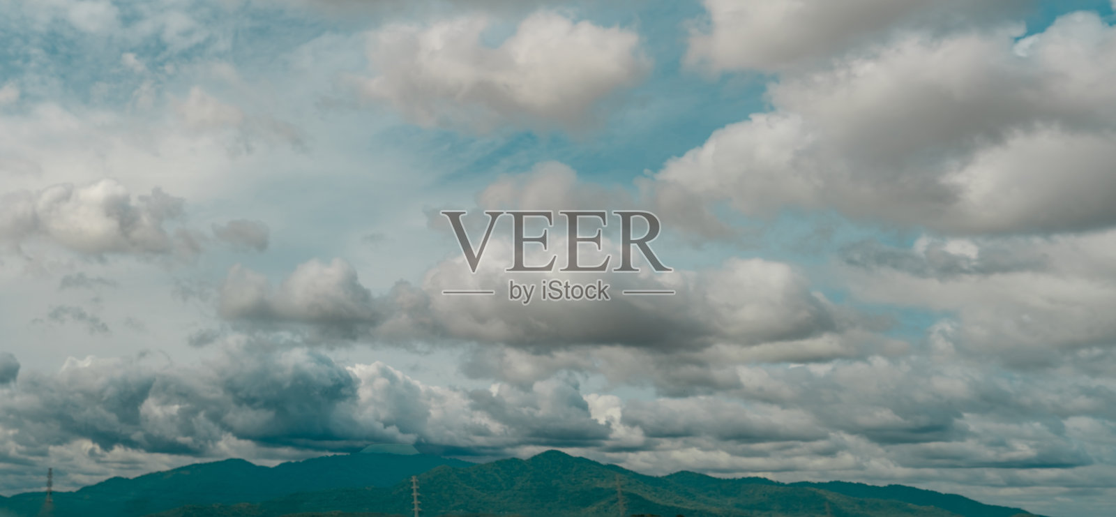 全景图的阴天上方绿色的山和电力塔。戏剧性的天空和积云。阴沉沉的天空。风暴的天空。Cloudscape。阴暗的云层。自然美。照片摄影图片