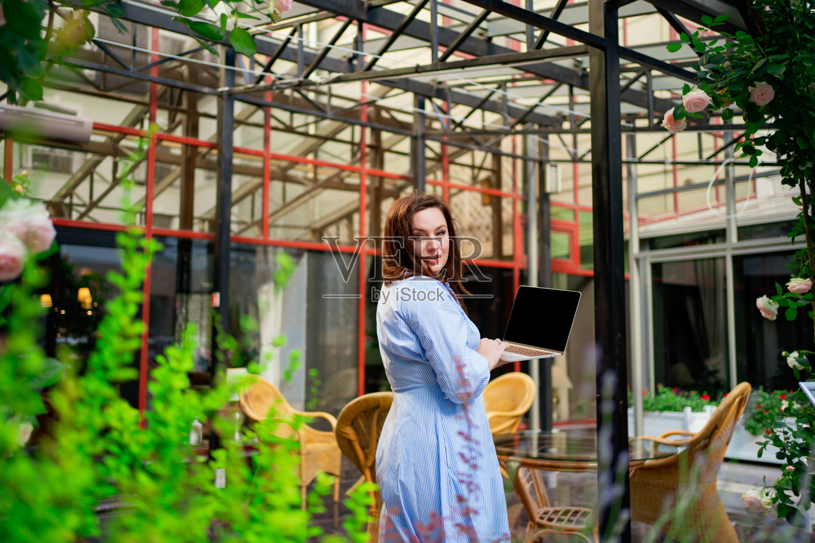 一个穿着蓝色裙子的漂亮女人在室外阳台上用笔记本电脑工作。照片摄影图片