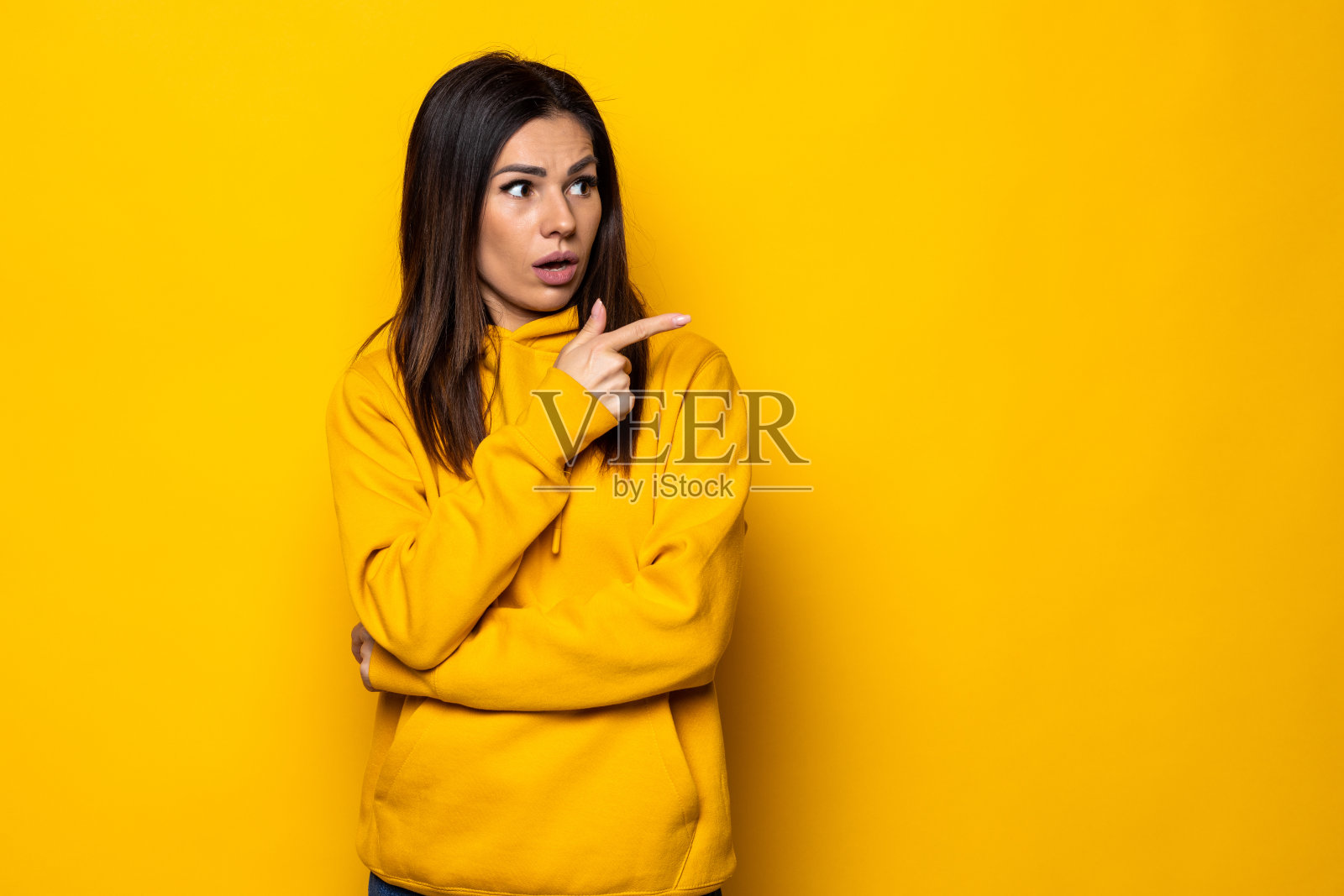 快活的女人一边看着一边指着黄色的背景。照片摄影图片