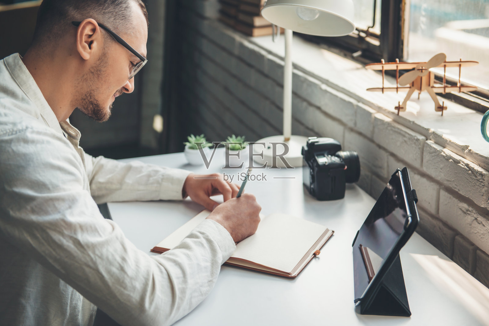 一名白人摄影师正在办公室用平板电脑和相机在抄写本上写东西照片摄影图片