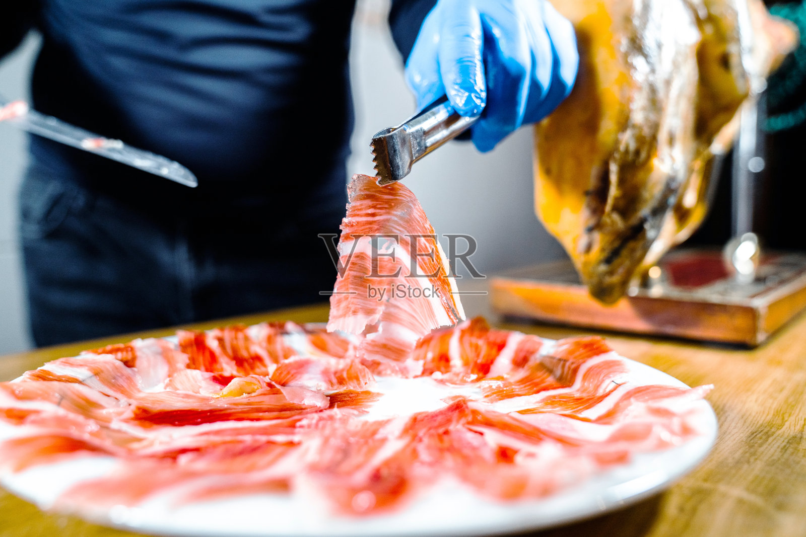 火腿板。开胃传统西班牙美味伊比利亚切片jamón或腌火腿腿。人拿着镊子。西班牙的美食。典型的西班牙或加泰罗尼亚食物。伊比利亚猪肉。照片摄影图片