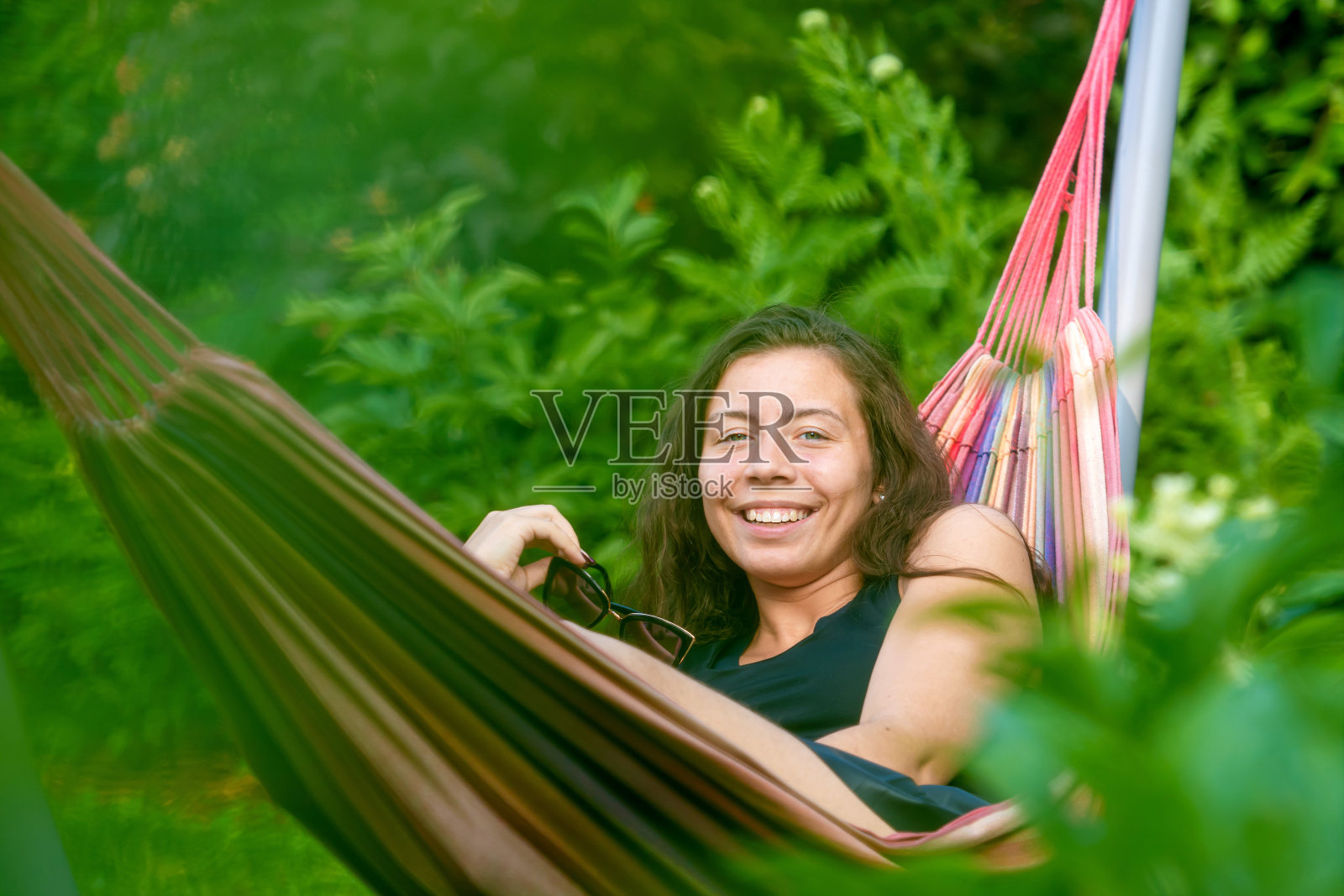 漂亮的女人戴着太阳镜躺在花园里的吊床上，放松，选择性聚焦照片摄影图片