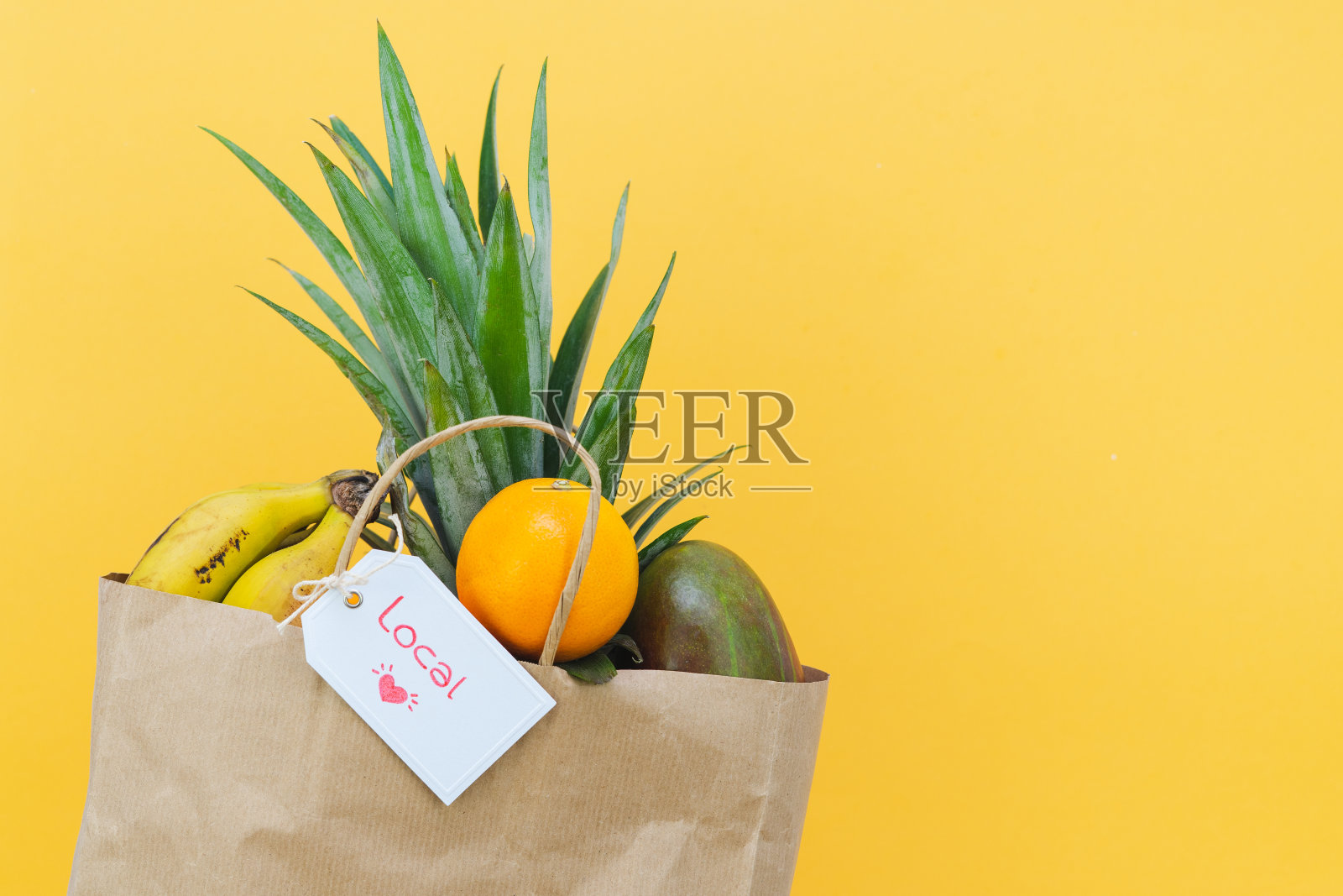 纸购物袋与热带水果和标签与字当地在黄色背景。副本的空间。照片摄影图片