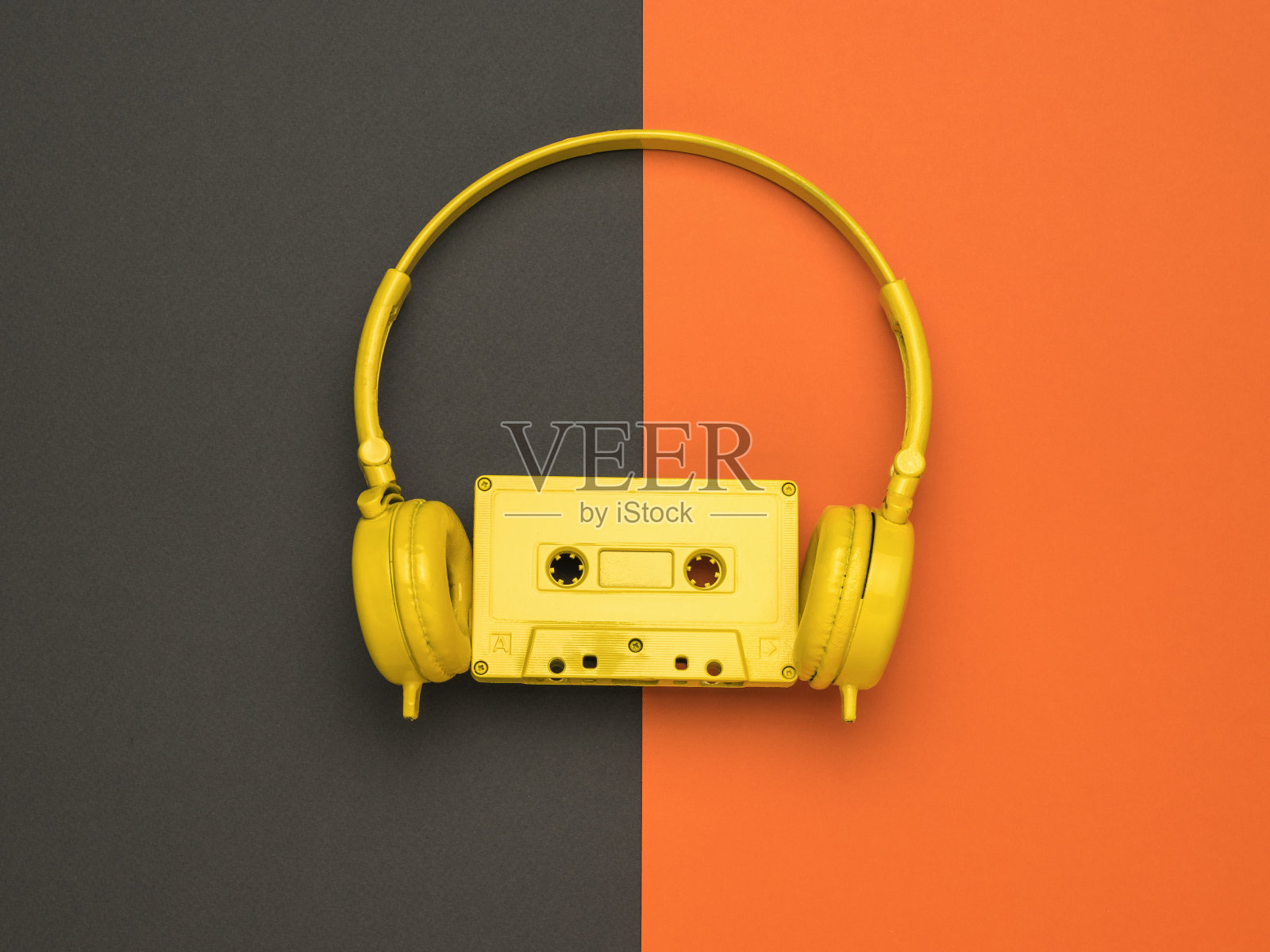一种橙色和黑色背景上带磁带和黄色耳机的黄色盒式磁带颜色的趋势。平的。照片摄影图片