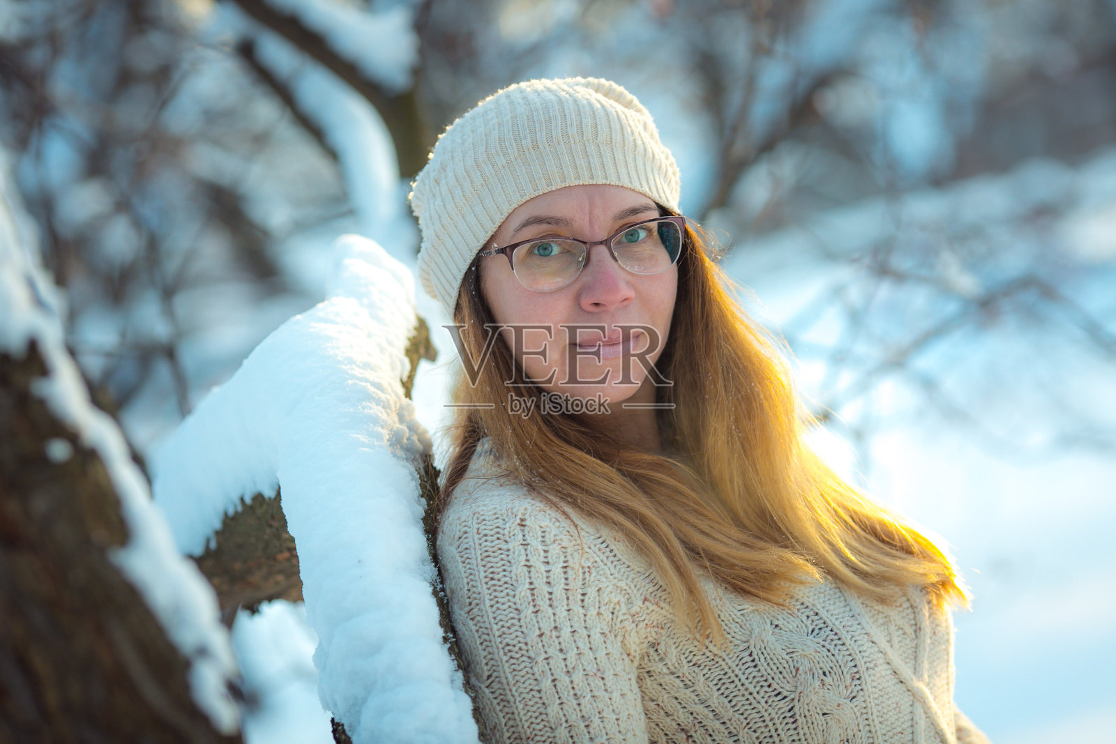 快乐的女人在阳光明媚的冬日里玩雪。女孩喜欢冬天，有霜冻的日子。在寒假玩雪，一个女人把白色的，松散的雪抛向空中。在冬天的森林里漫步。照片摄影图片