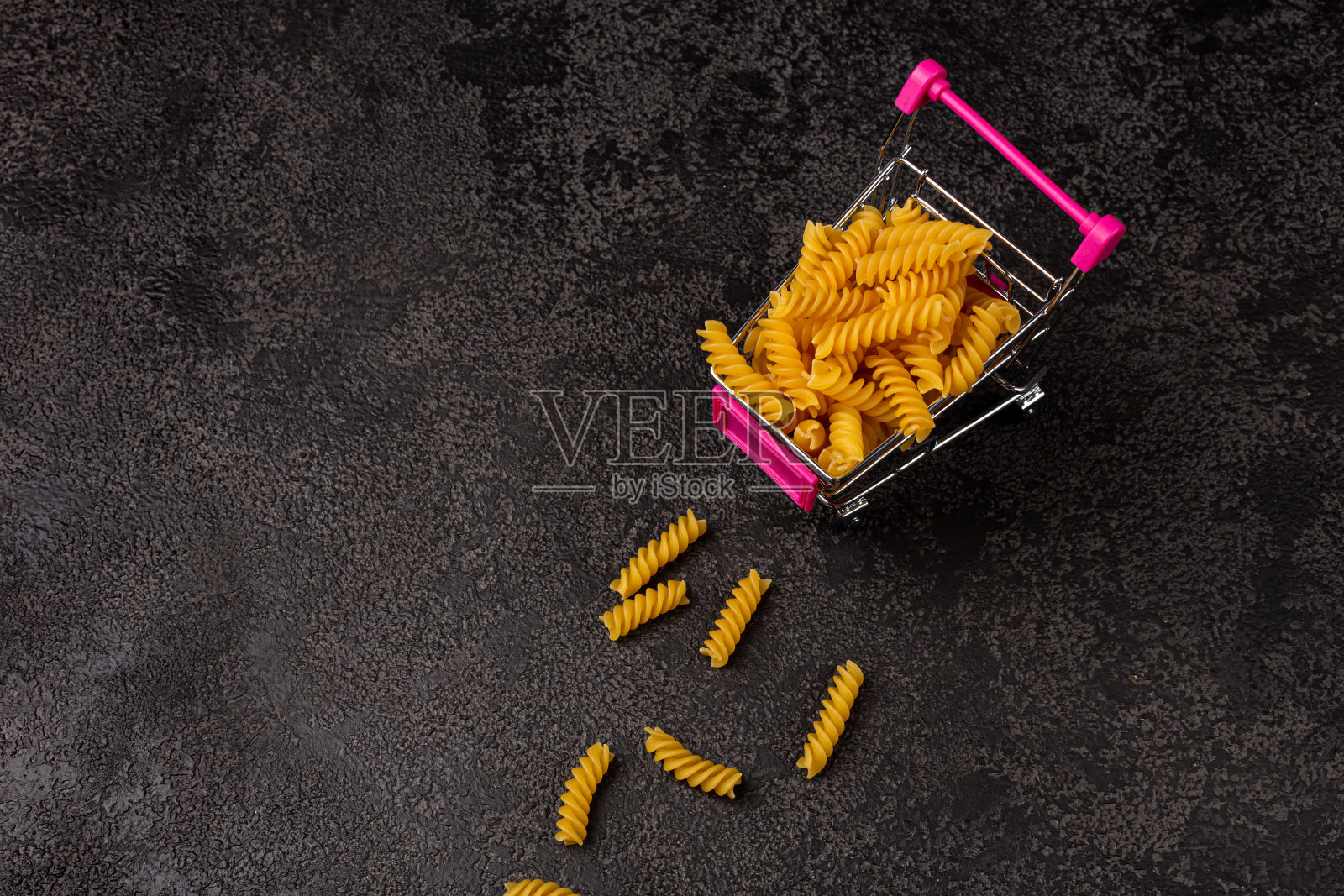 一堆生的黄色意大利面，在黑暗的结构背景上，有空间复制。前视图。通心粉在推车里照片摄影图片