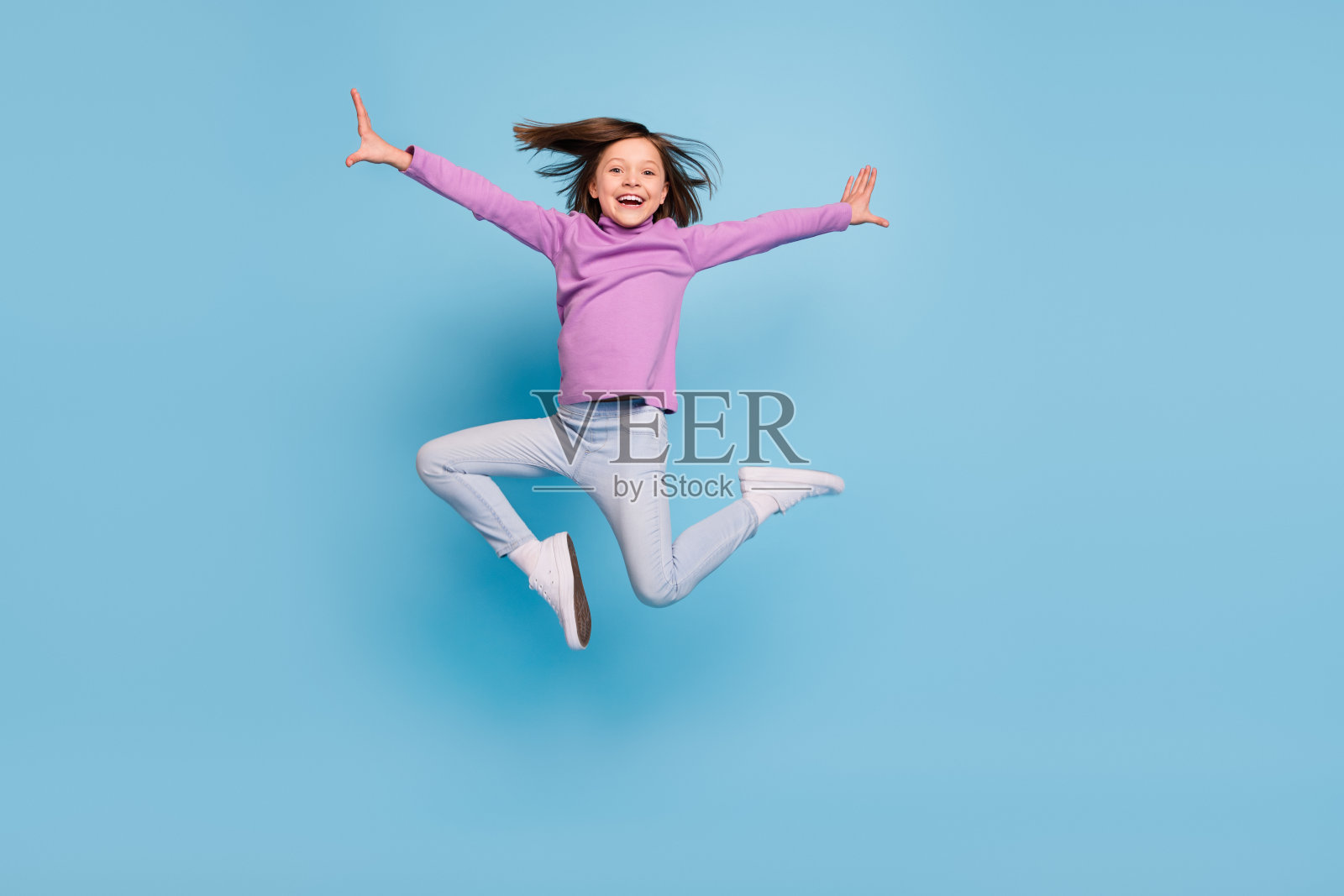 可爱有趣的小女生穿着紫色高领微笑跳高孤立的蓝色背景的照片照片摄影图片