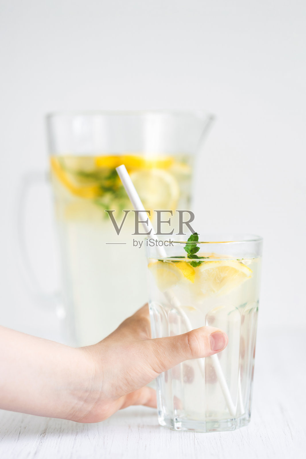 白色的桌子上放着玻璃杯和一大罐柠檬水。照片摄影图片