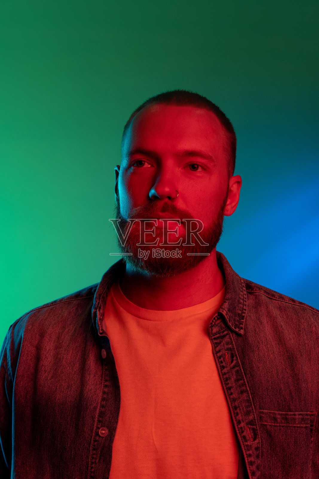 近距离的肖像，年轻的白人胡须男子孤立在梯度绿蓝色背景霓虹灯。照片摄影图片