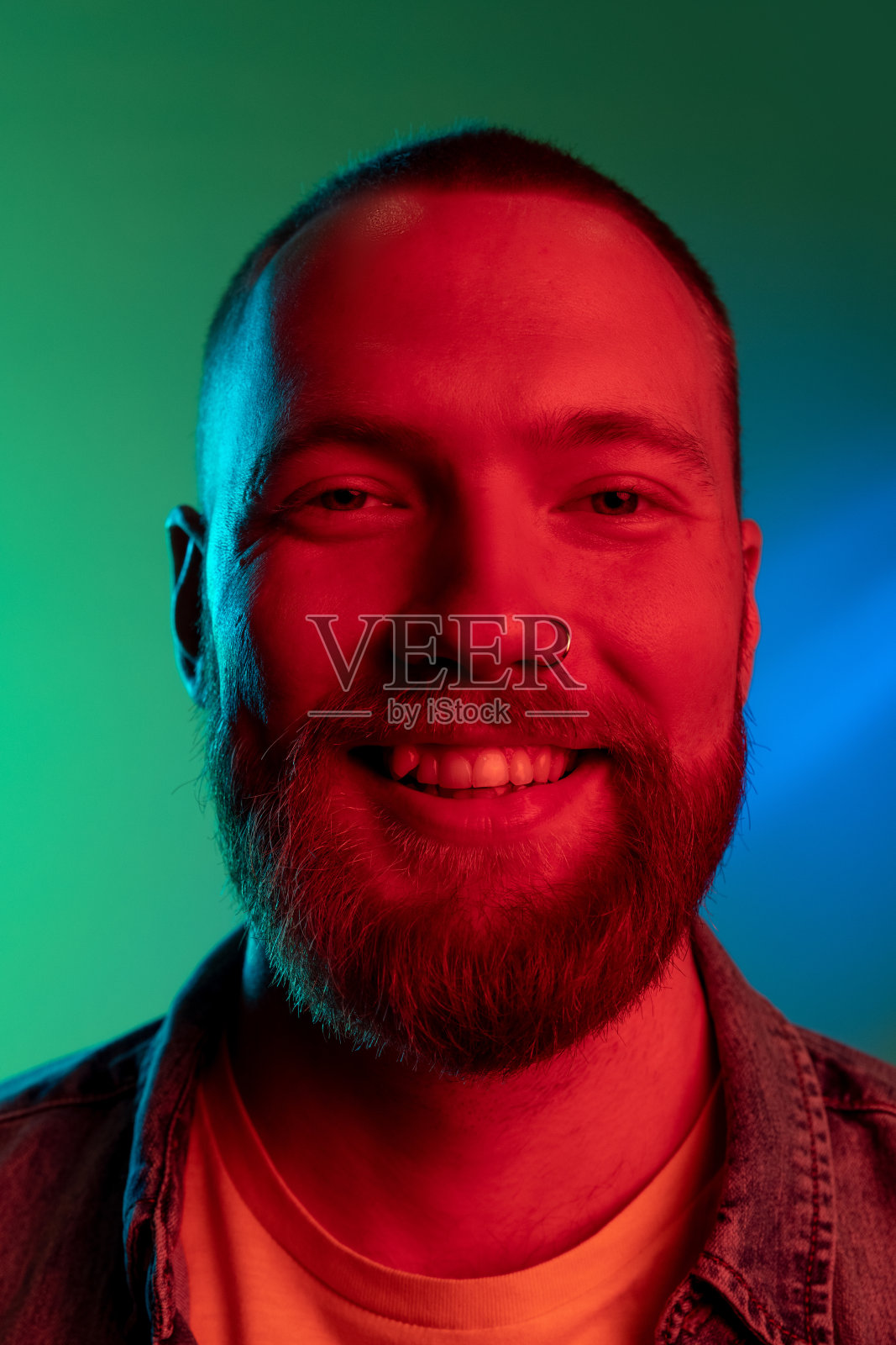 近距离的年轻英俊的微笑白人男子孤立在绿色背景在蓝色霓虹灯。照片摄影图片