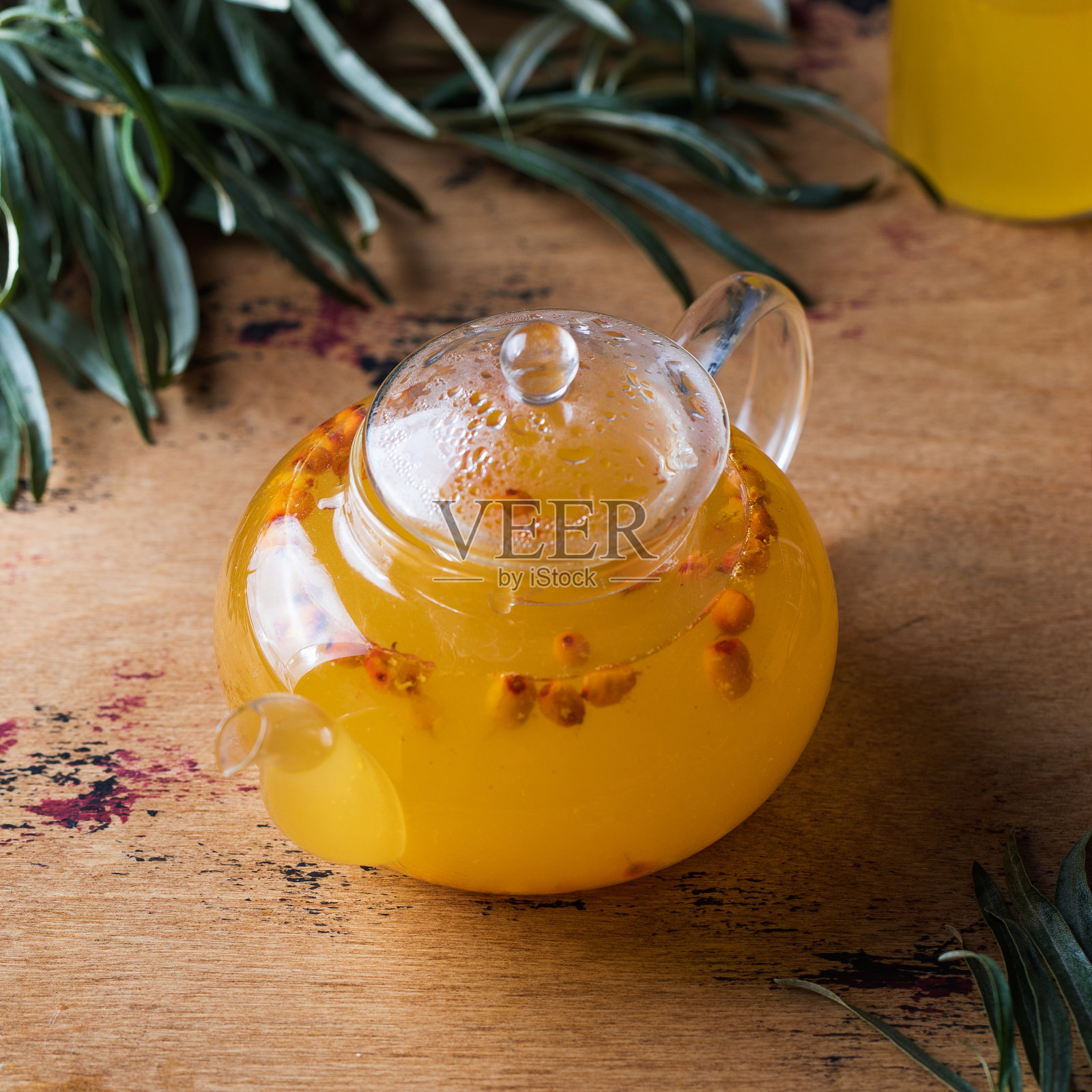 透明茶壶与沙棘茶在一个木制的背景。秋茶。照片摄影图片