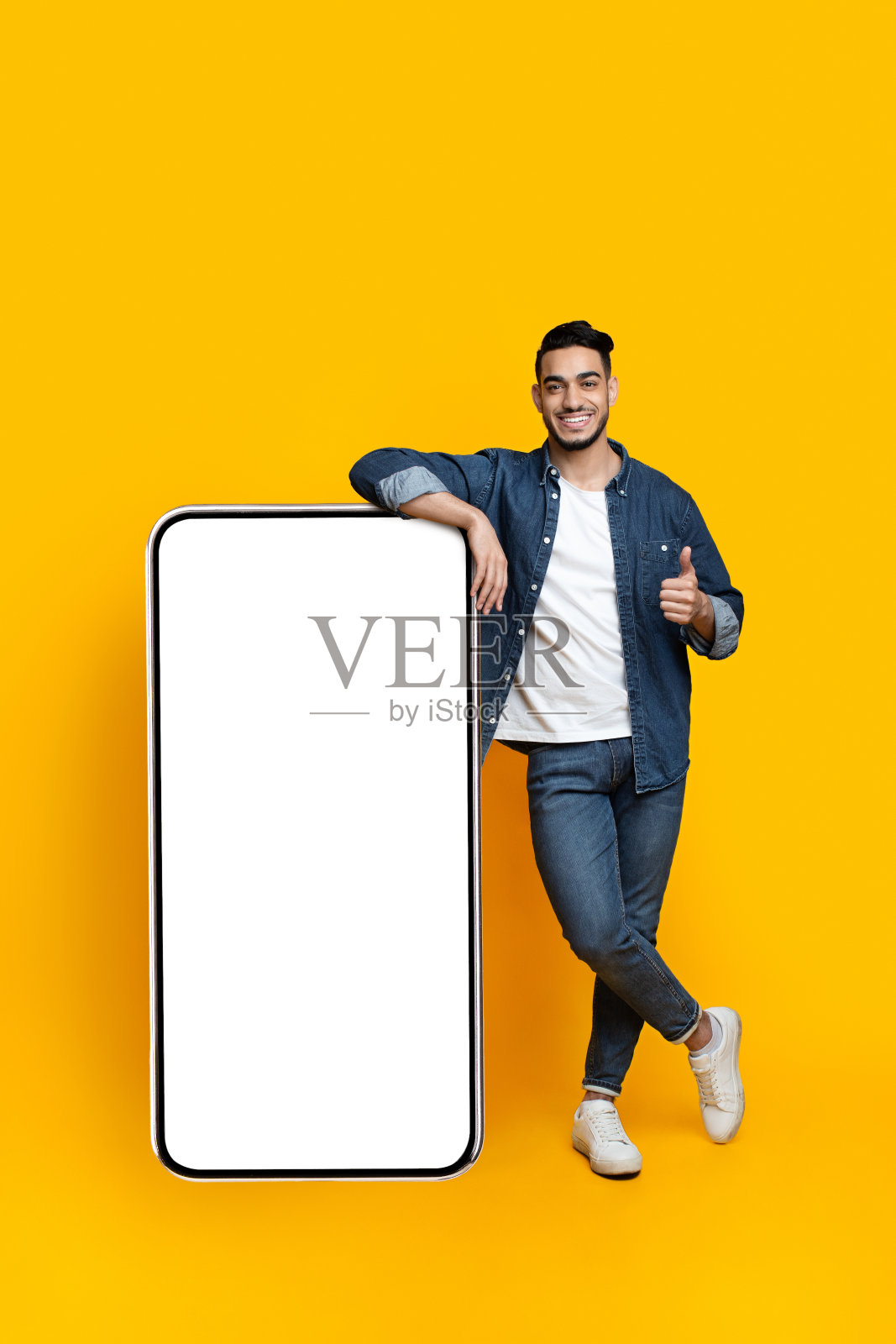 靠在巨大智能手机上的快乐阿拉伯男人，模型照片摄影图片