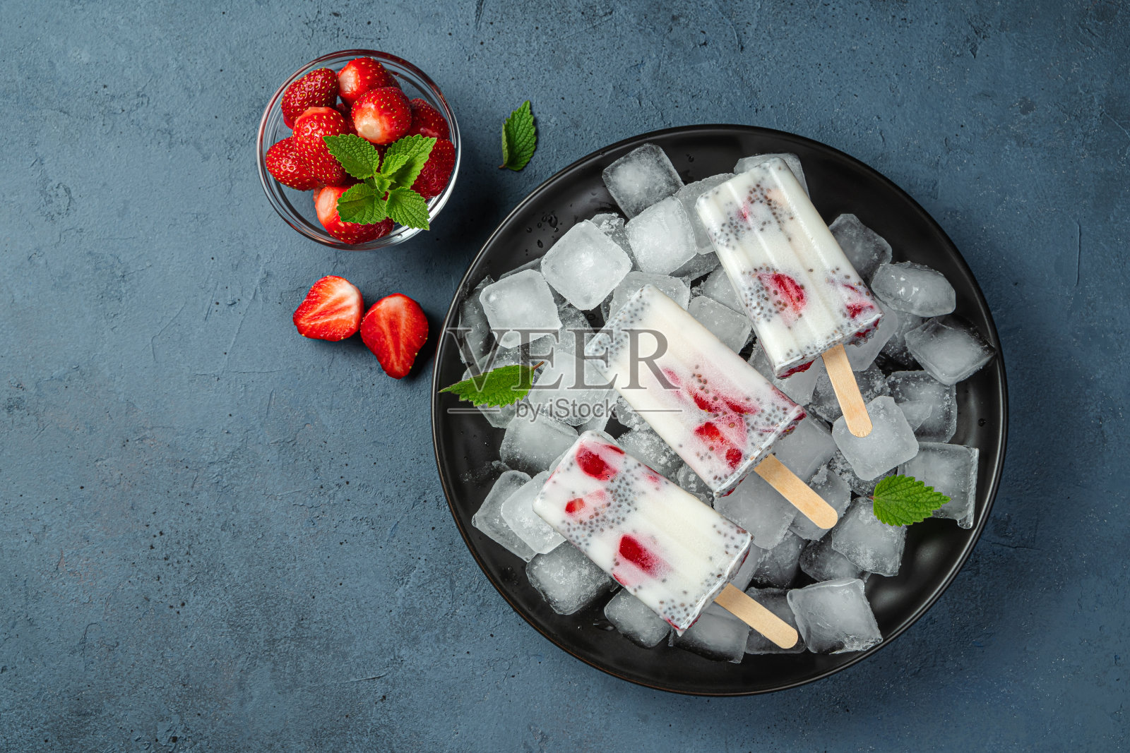 健康的自制冰淇淋，配上草莓、奇异籽和薄荷，放在黑色的盘子里，在深蓝色的背景上照片摄影图片