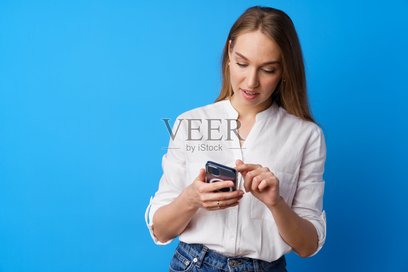 年轻的金发女子使用她的智能手机在蓝色背景的特写照片摄影图片