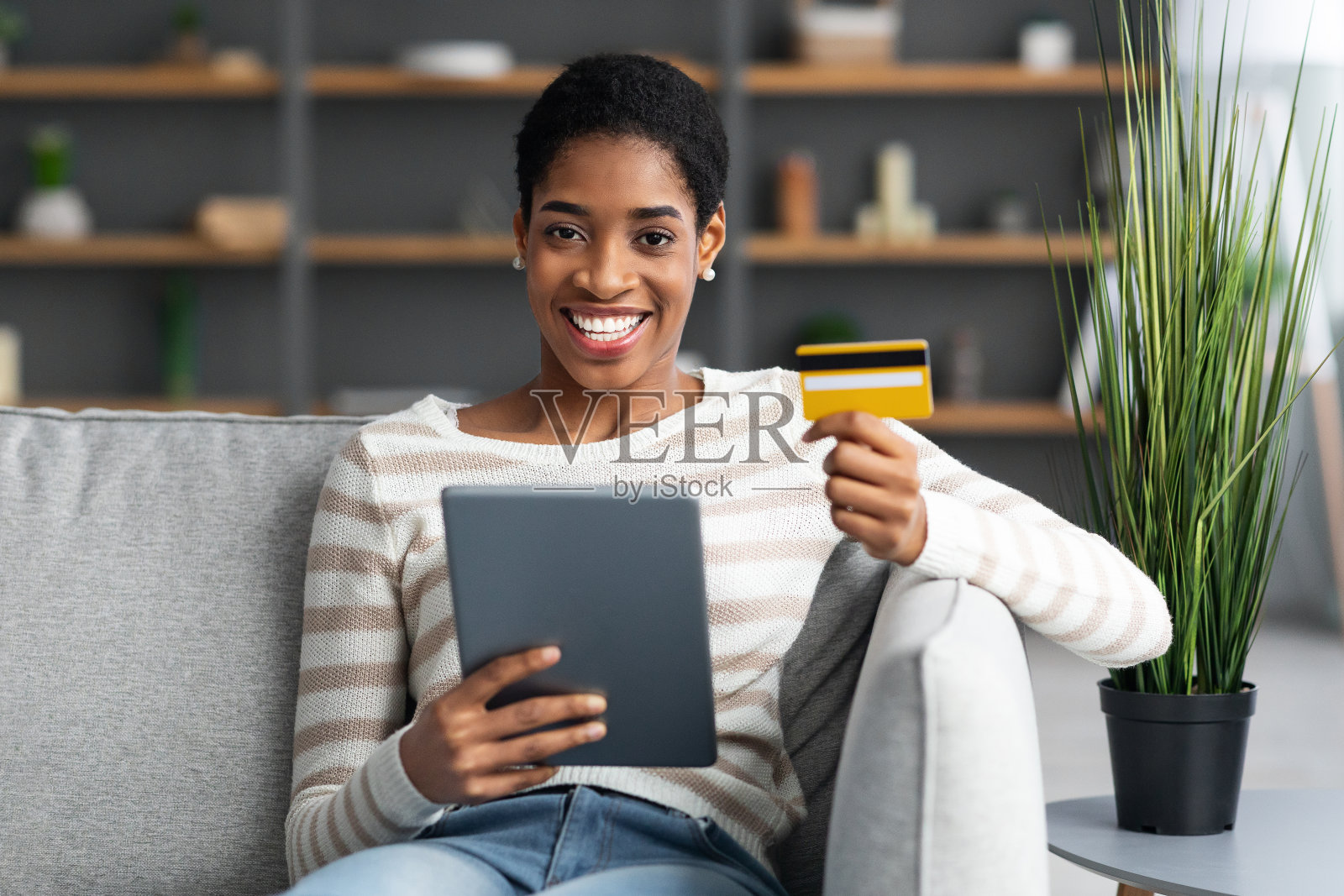 微笑的黑人妇女使用数字平板电脑和信用卡进行网上购物照片摄影图片