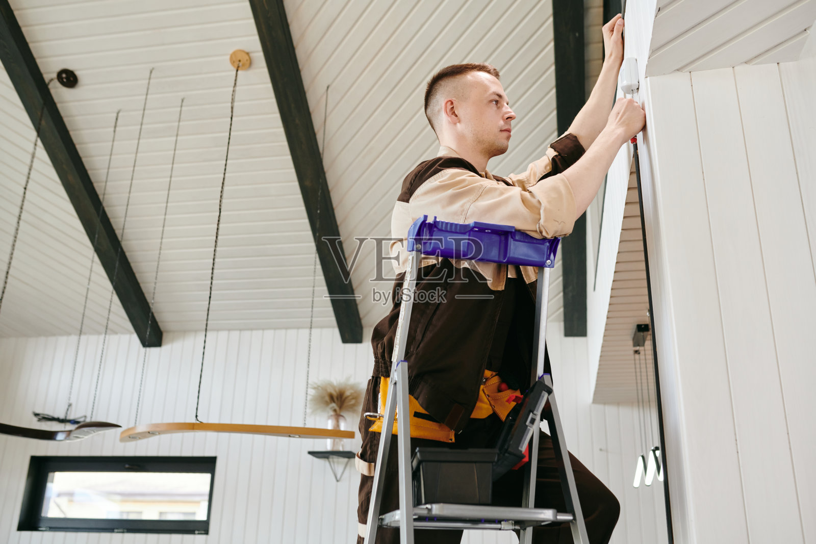 穿着制服的年轻工人正在安装房子的报警系统照片摄影图片
