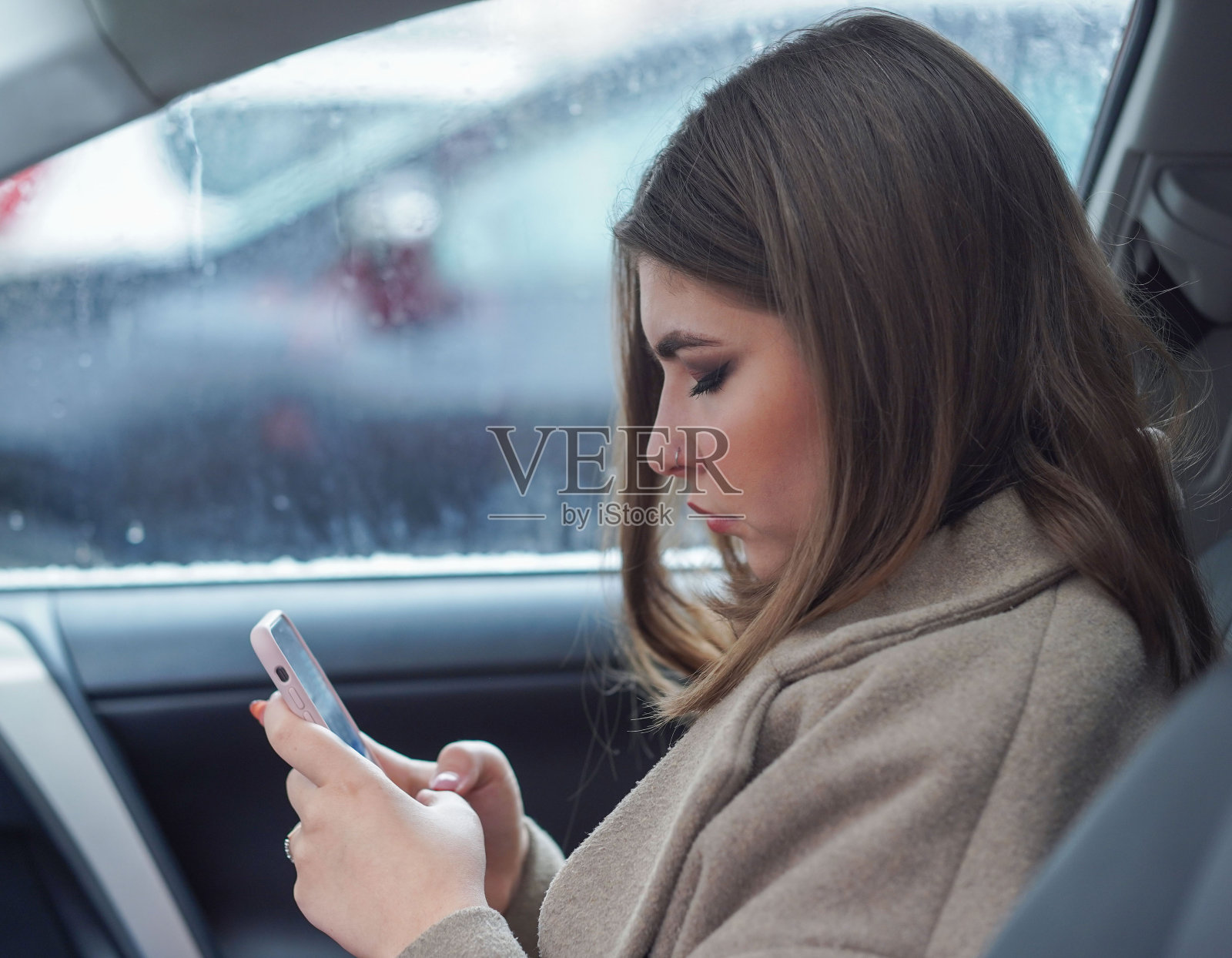 兴奋的年轻女商人坐在车里，看着她的手机。一个女人在看手机短信。照片摄影图片