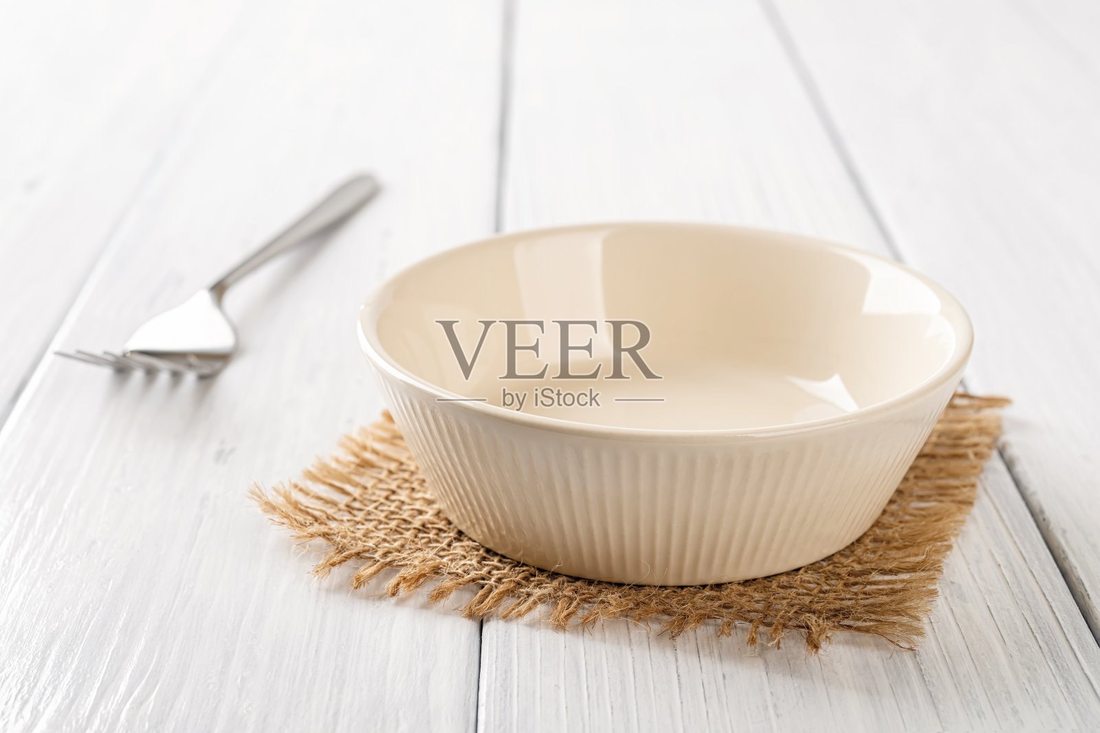 白色木桌上放着米色的空碗和金属叉子。桌子上一个干净的瓷碗。用于食物设计模型的空陶瓷餐具模子。高音调的形象。照片摄影图片