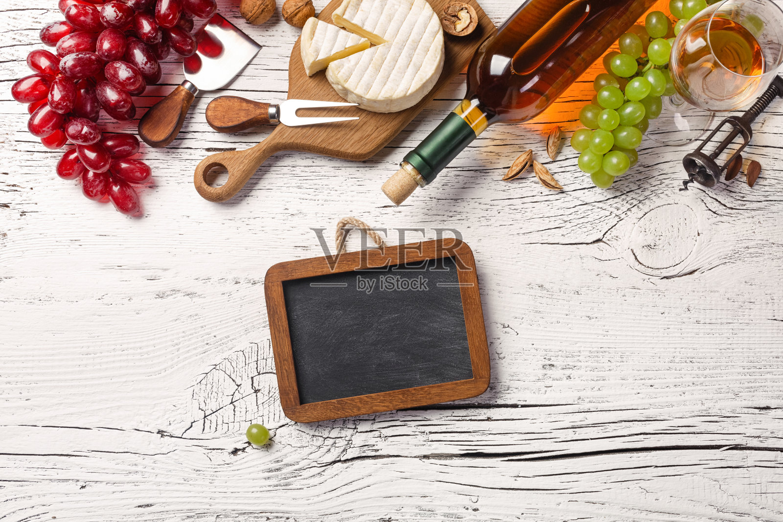 白酒瓶，葡萄，蜂蜜，奶酪，酒杯和白色木板上的黑板照片摄影图片