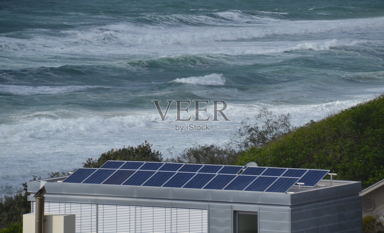房屋屋顶上的太阳能光伏板以海浪为背景照片摄影图片
