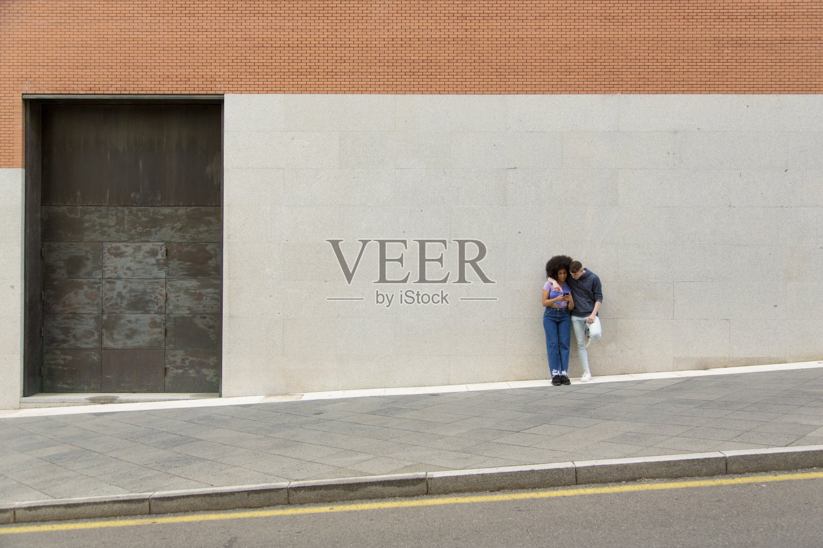 年轻的白人男子和黑人妇女使用手机在城市与背景墙与复制空间照片摄影图片