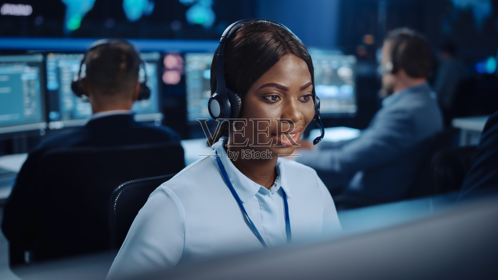 在电话中心控制室里，满是同事、显示屏和数据服务器，技术客户支持专家一边用耳机说话，一边用电脑工作。照片摄影图片