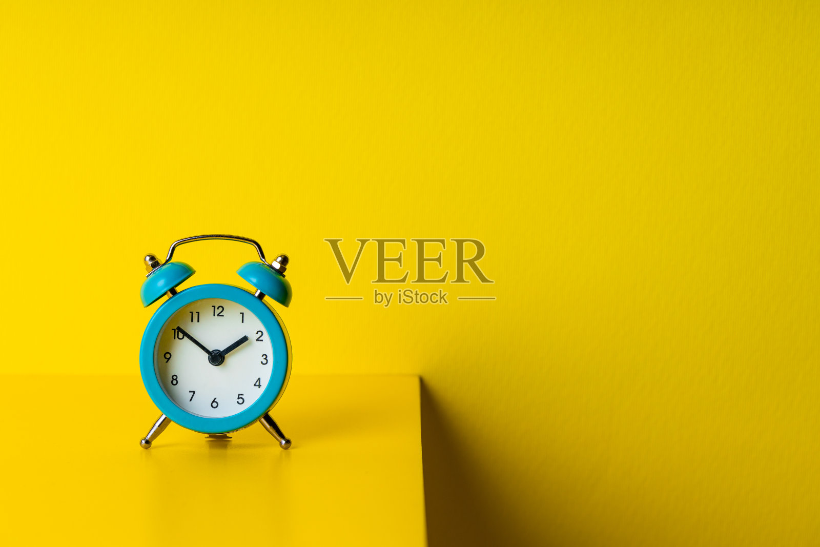 蓝色的闹钟放在黄色的桌子和黄色的墙壁背景上。副本的空间。抽象的时间概念照片摄影图片