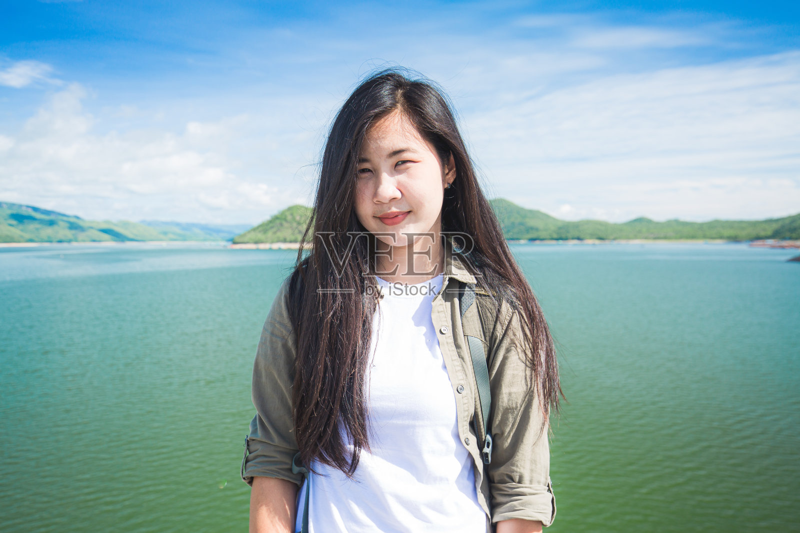 年轻幸福的女子背着双肩包，高举双手站在河边。女性旅游的概念照片摄影图片