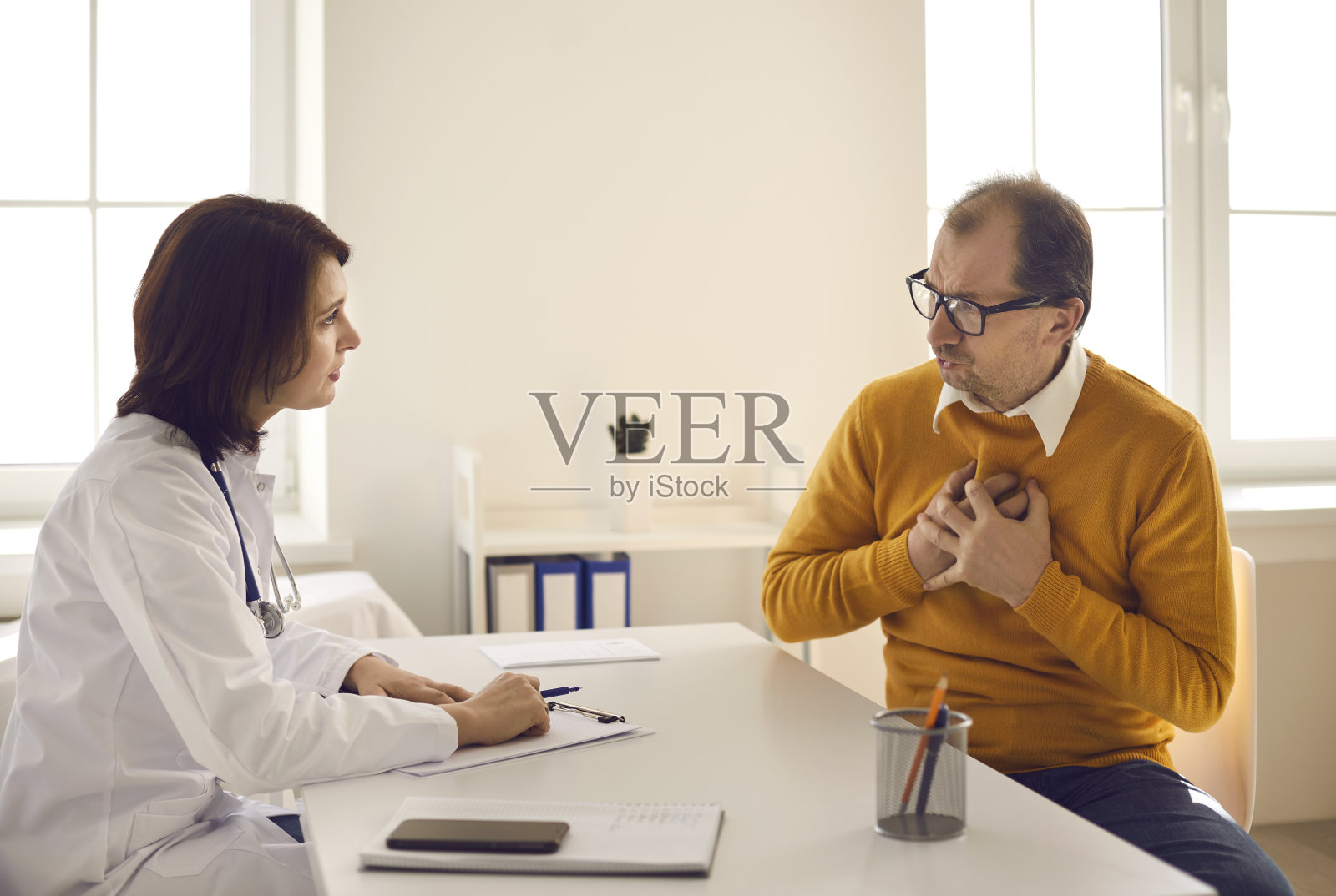 成年患者坐在桌前，与医生交谈，抱怨胸痛照片摄影图片