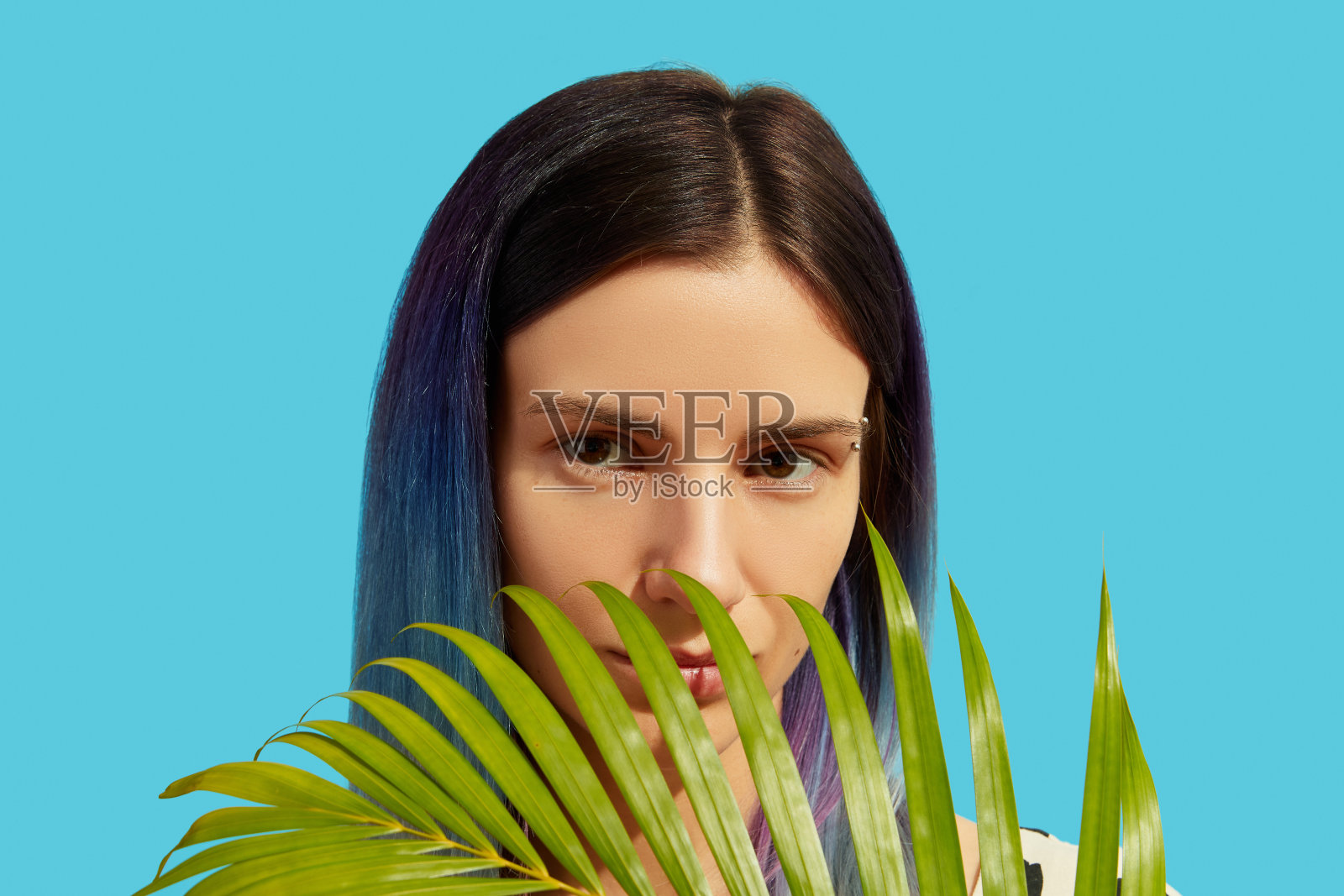 在明亮的背景上，一个年轻美丽的女子，有着蓝色的头发，手里拿着棕榈叶照片摄影图片