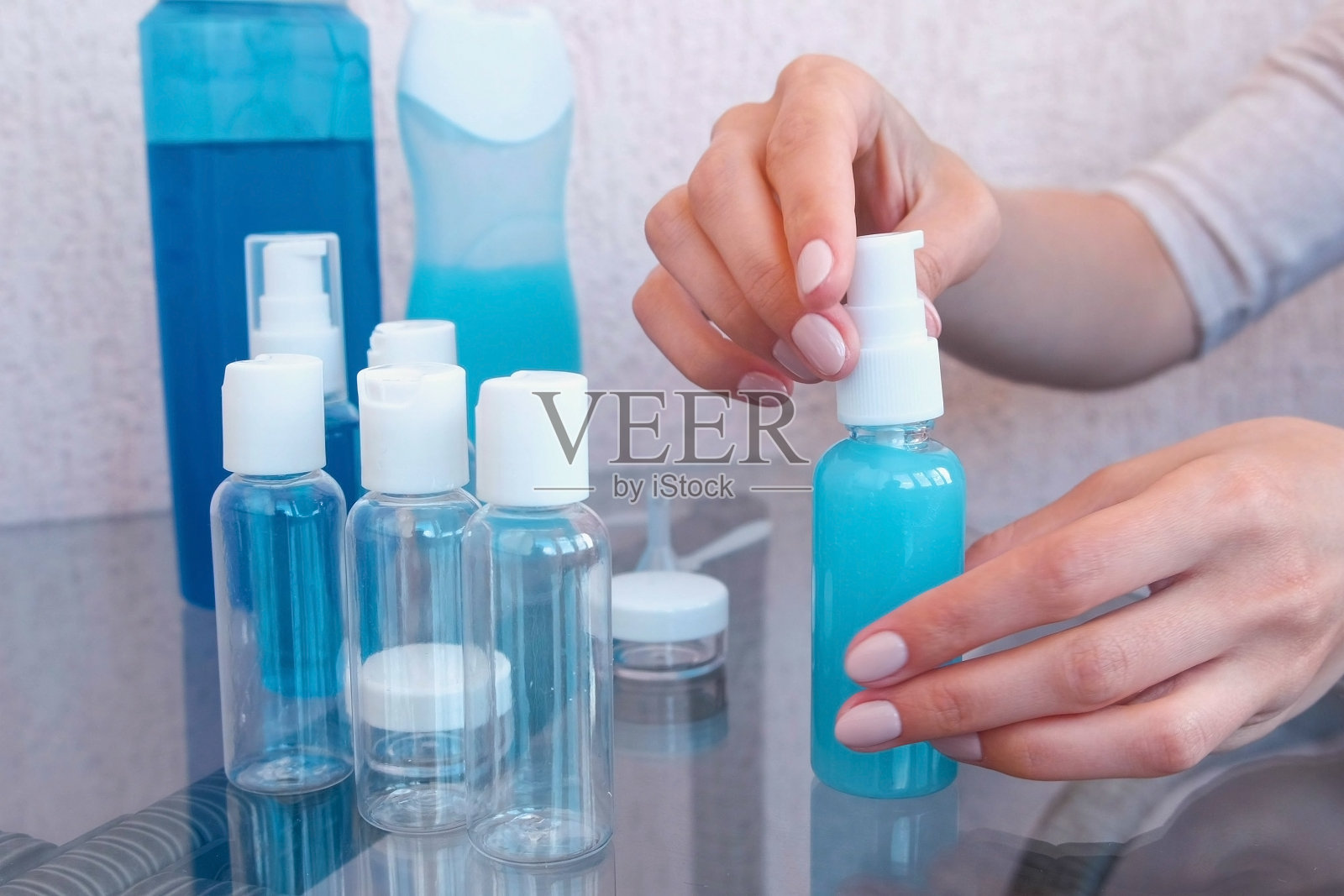 女人的双手拧上了一小瓶沐浴露。旅行罐。照片摄影图片