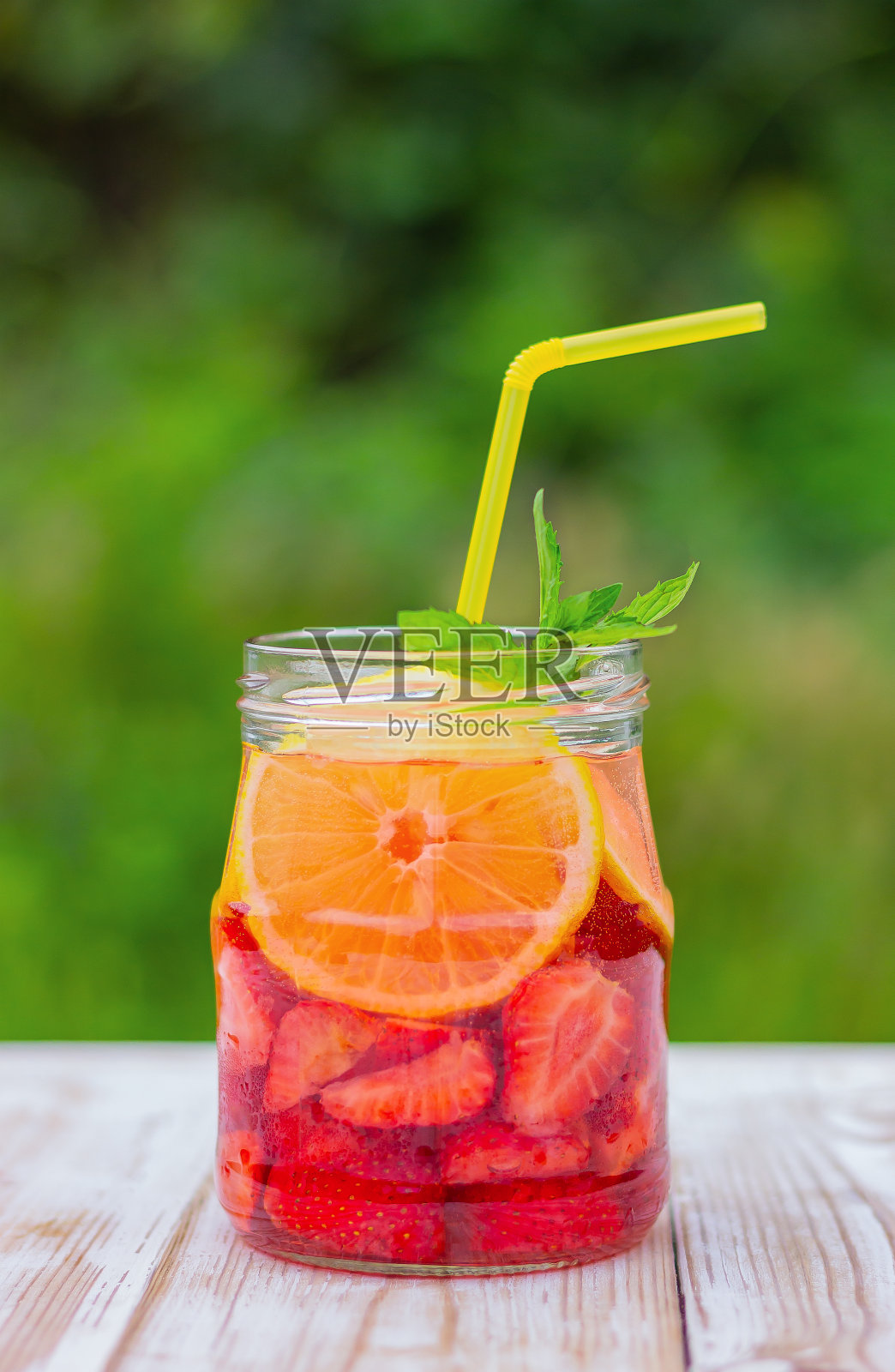 花园里的桌子上放着柠檬、草莓和薄荷饮料。照片摄影图片