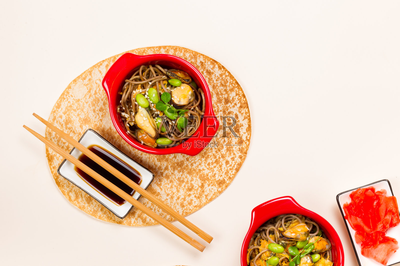 两份荞麦荞麦面配蔬菜和贻贝。盛在红碗里，配上筷子和皮塔饼。平铺在米色背景与空间的副本照片摄影图片