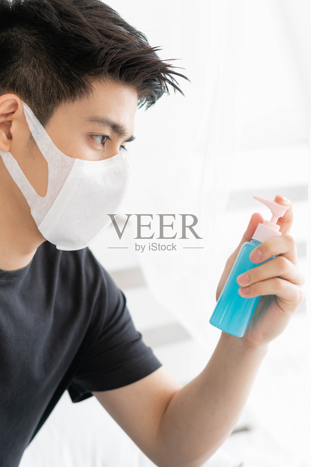 亚洲男子在隔离室内戴口罩，手持酒精洗手以保护新冠病毒，隔离自己以防止新冠病毒传播照片摄影图片