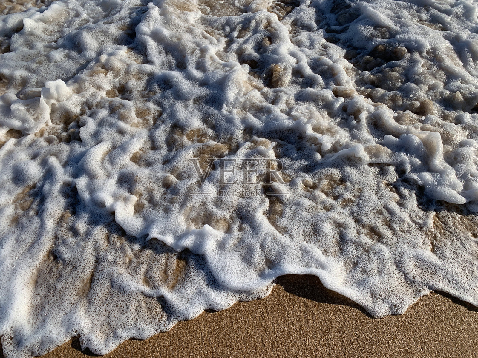海水泡沫沿着海滩的沙质海岸爬行照片摄影图片