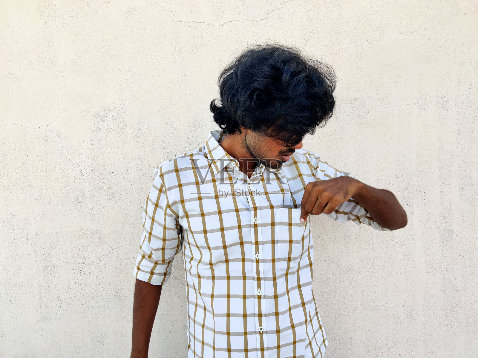 一个留着长发的年轻人用左手检查他的衬衣口袋。没有钱或拿钱照片摄影图片