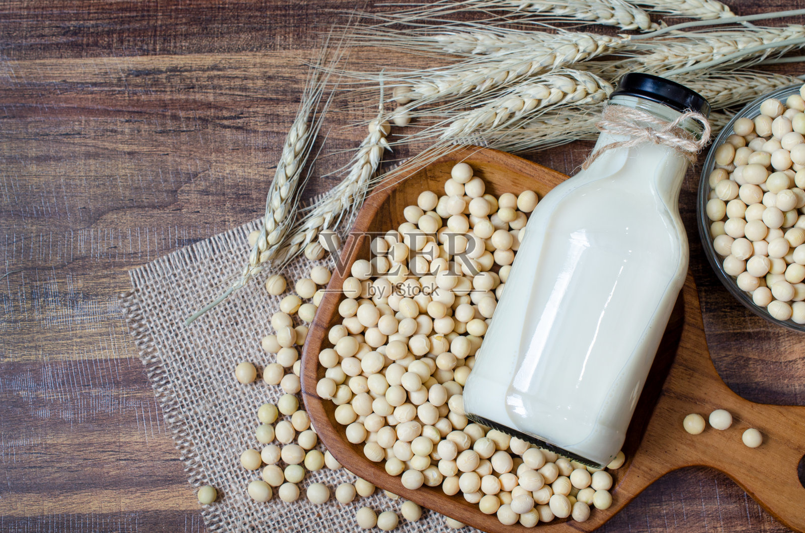 俯视图干燥的有机自制豆浆在玻璃瓶和一些种子在木碗上布袋织物和干小麦穗在深棕色的木制背景照片摄影图片