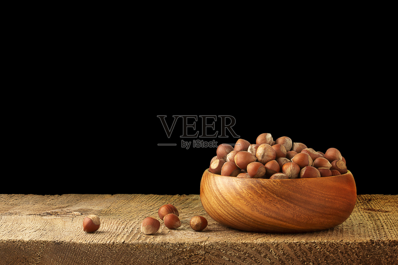 坚果，榛子装在一个木碗里放在一张黑色的桌子上。健康食品的概念。照片摄影图片