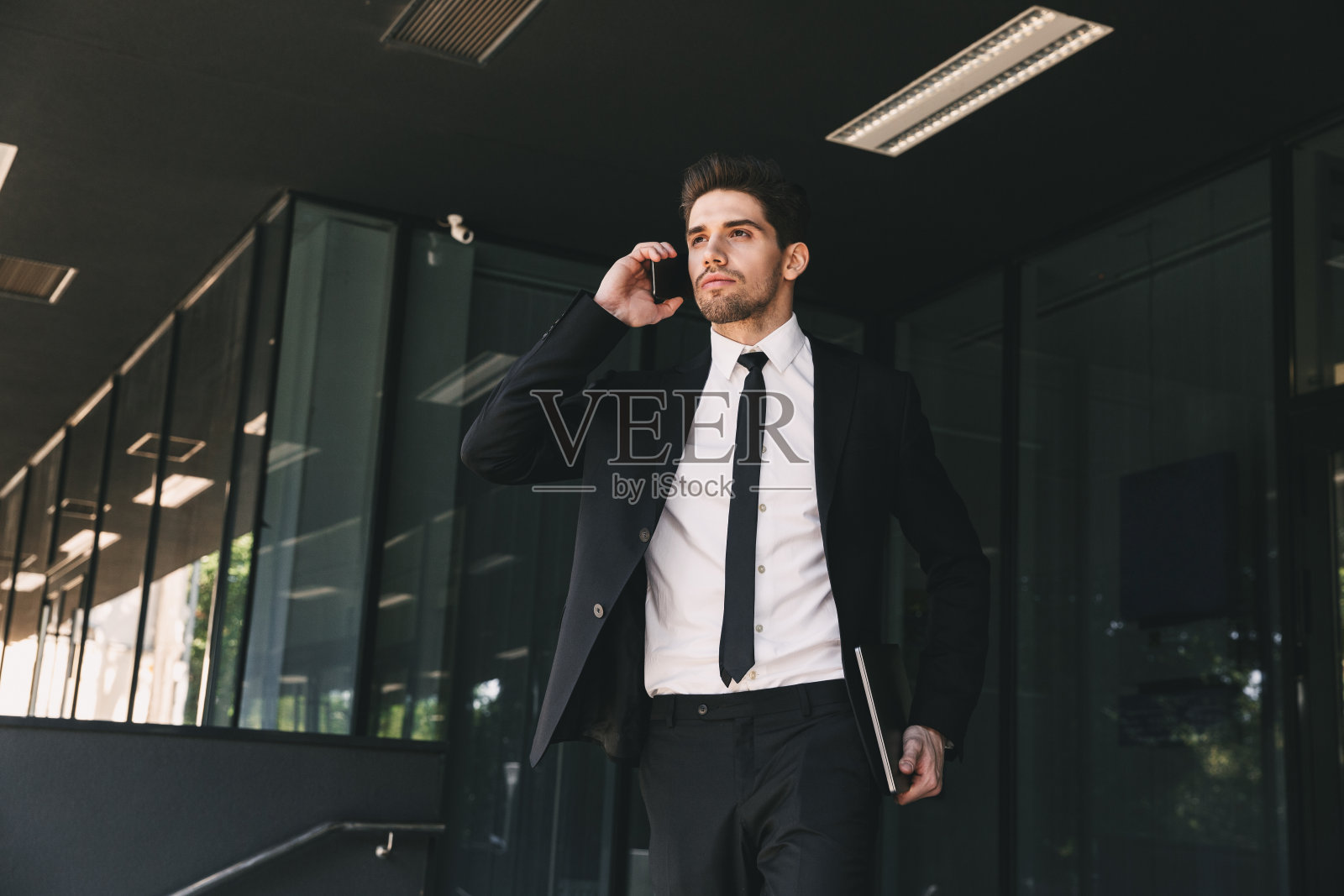 一幅年轻商人的肖像，穿着正装站在玻璃建筑外，用智能手机讲话照片摄影图片