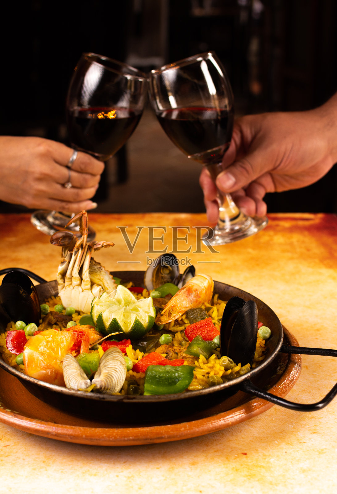 在餐馆里，两只手举着红酒和海鲜饭向两个面目全非的人敬酒照片摄影图片