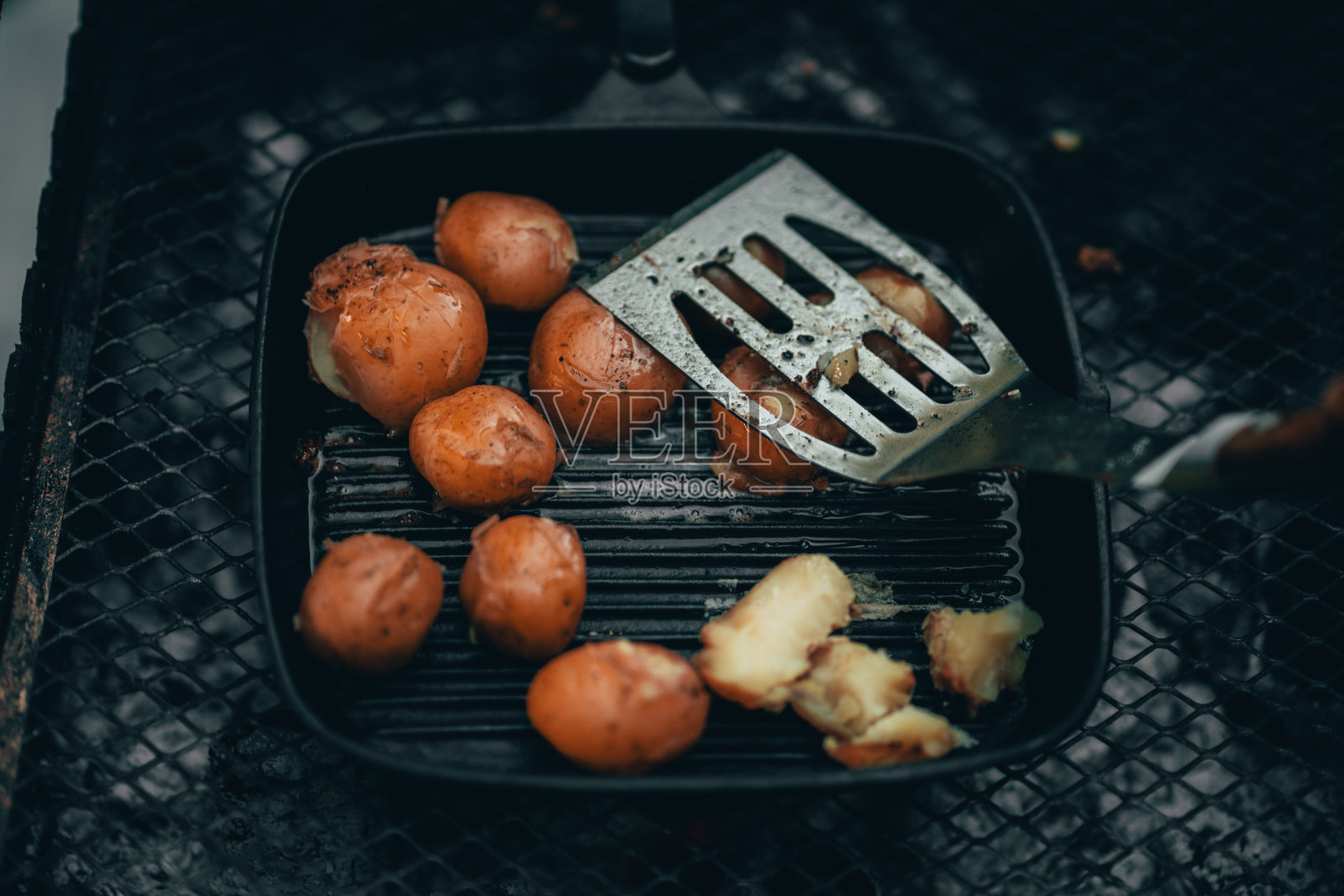 在铸铁煎锅中还处于烹饪阶段的年轻炸土豆被烤好，并用铲子压紧照片摄影图片