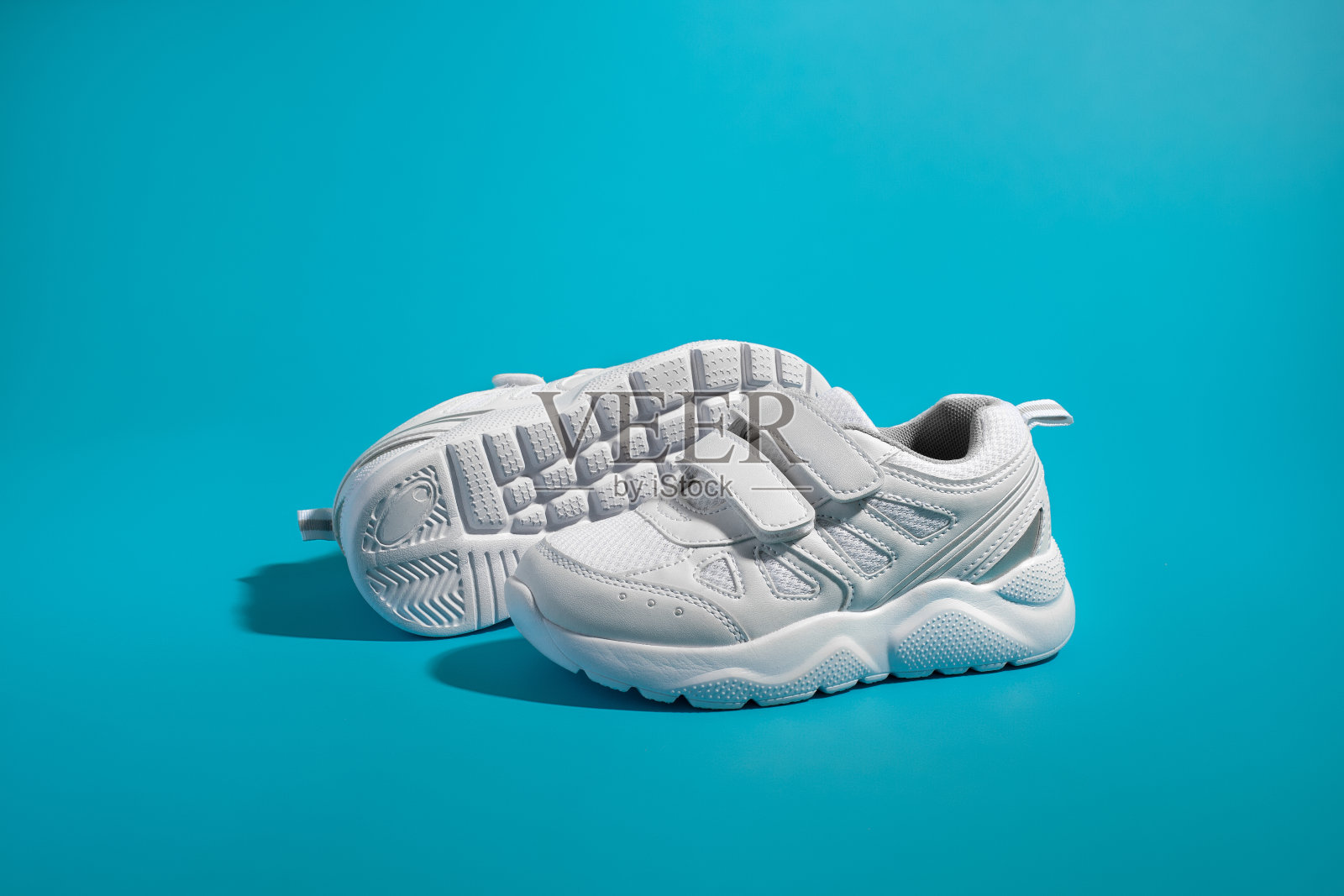 侧视图的一个白色男女皆有的运动鞋与尼龙搭扣站在前面的另一个运动鞋的鞋底在一个孤立的蓝色纸背景照片摄影图片