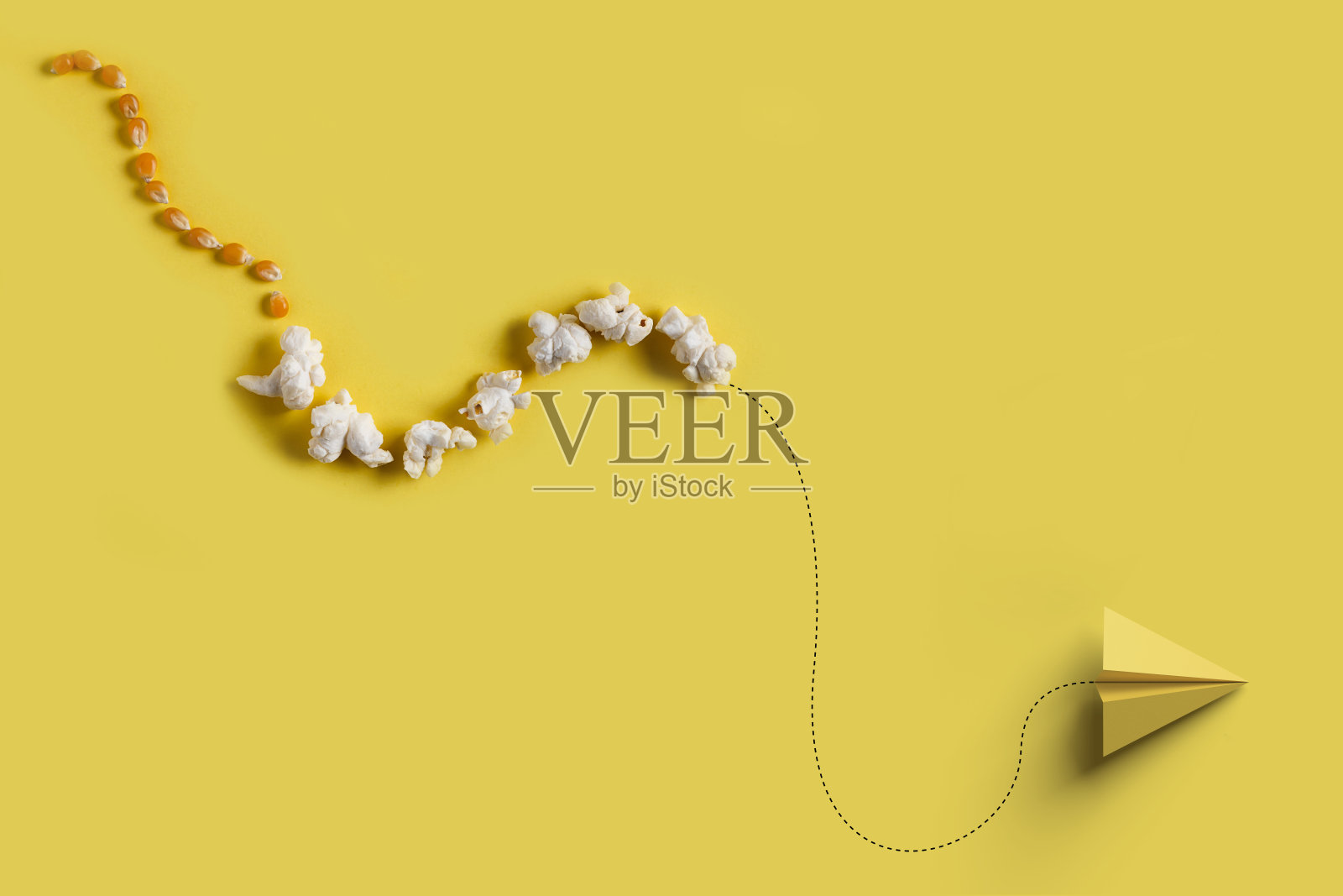 纸飞机在黄色的背景上飞行着一排玉米粒和爆米花。照片摄影图片