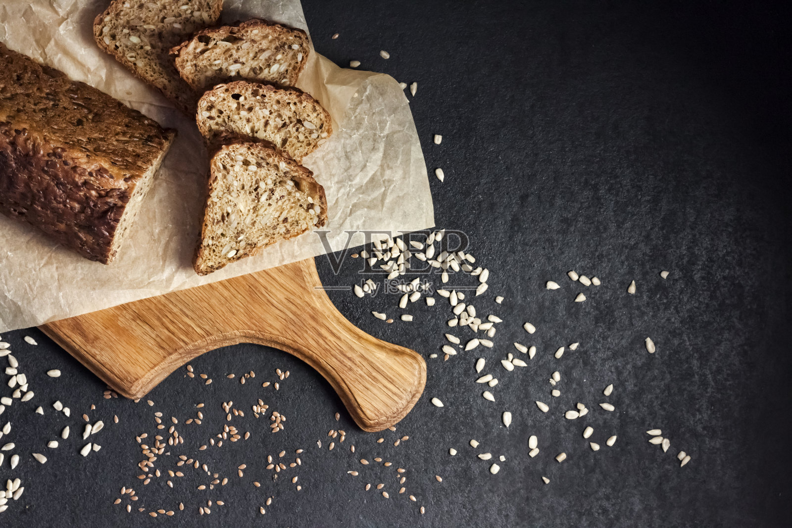 在黑色背景的木制砧板上，面包上有向日葵和亚麻籽照片摄影图片