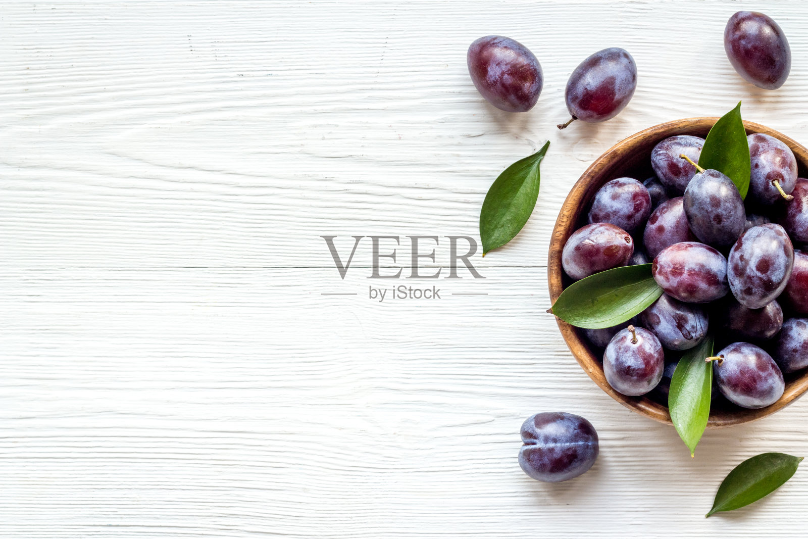 碗里的成熟的李子。带叶子的樱桃果。俯视图照片摄影图片