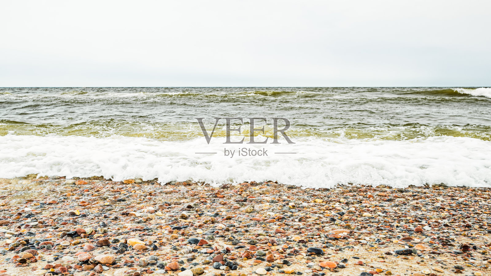 沙滩上有各种各样的海岩石，背景是不安的波罗的海和波浪照片摄影图片