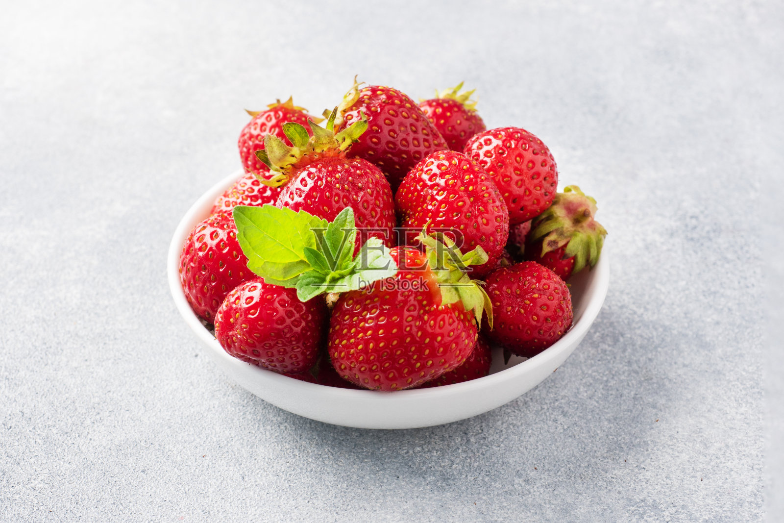 混凝土背景下的盘子里装着熟透多汁的草莓。香甜健康的甜品，维生素丰收。副本的空间。照片摄影图片